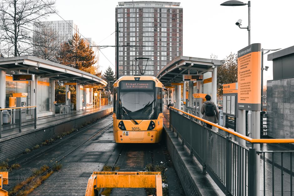 A broad external staircase with multiple steps leading up to the entrance of Surrey Quays Station, featuring black rubber treads with yellow safety strips along the edges of each step. The stairs are 